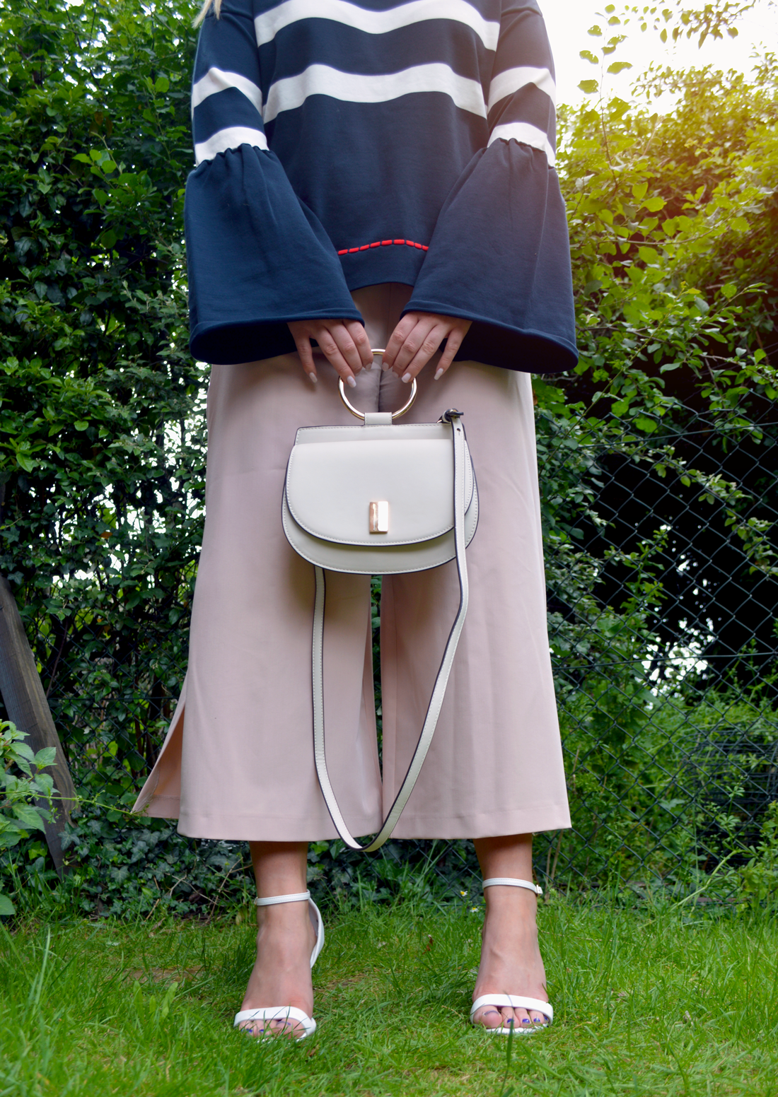 Hannah Gladwin wearing Asos nude culottes with side splits, with barely there white heeled sandals, with an over-sized navy knitted jumper with large sleeves, holding a cream Mango bag by its gold ring.