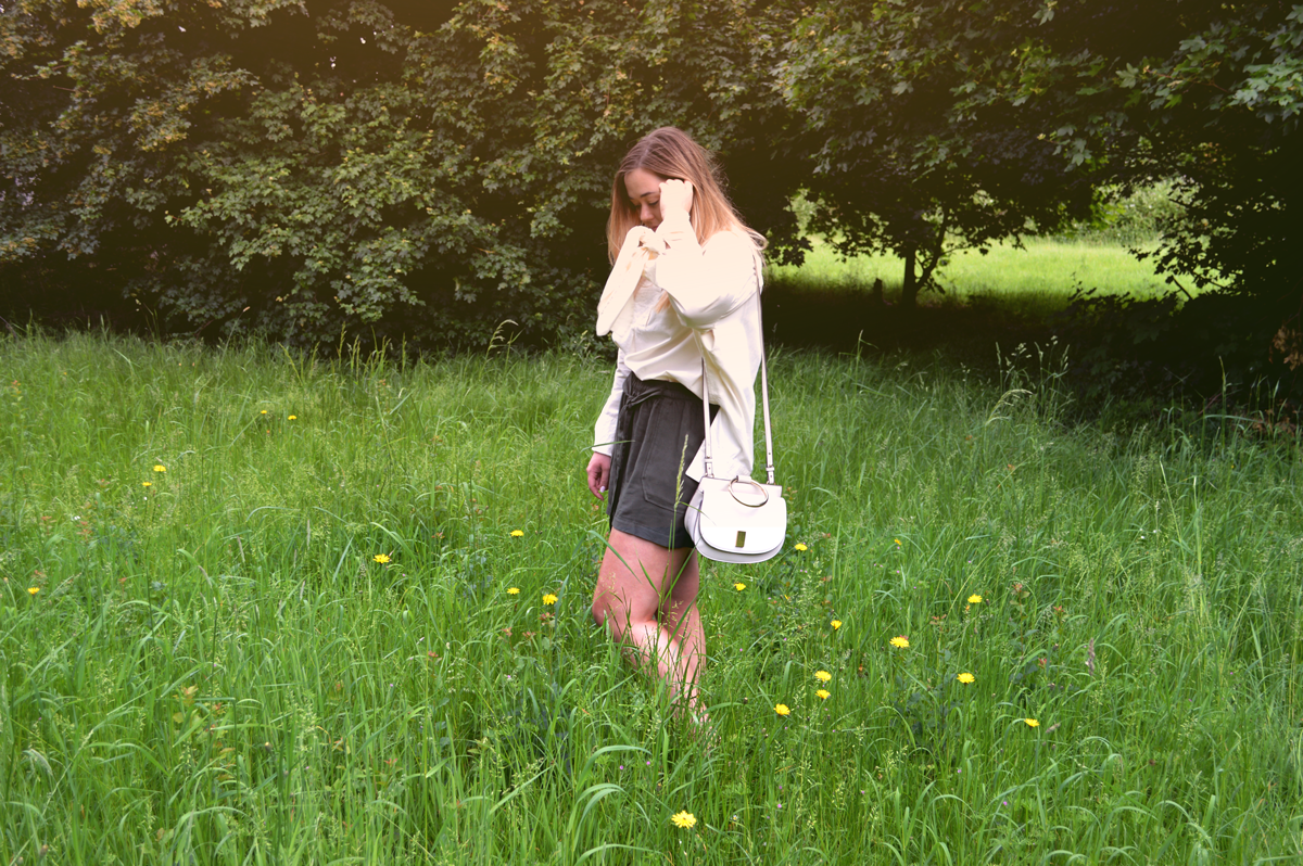 Hannah wearing Mango over-sized cream shirt with bows hanging down with khaki baggy shorts in a field on a sunny day.